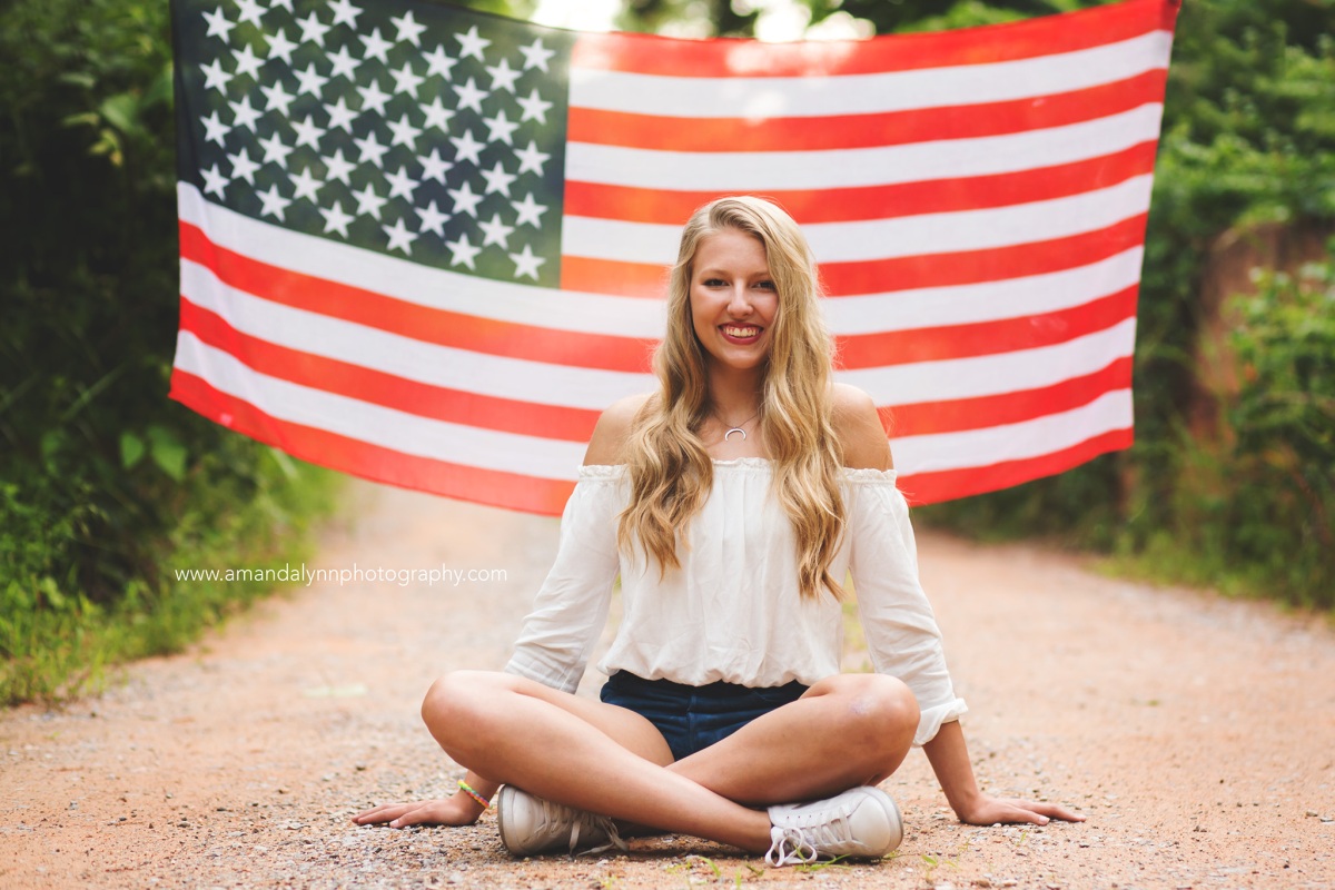 2017 Senior Rep for Amanda Lynn Photography Oklahoma City sitting on dirt road in front of American Flag